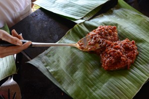 Man wickelt man den mit Sauce bedeckten Fisch in Bananenblätter